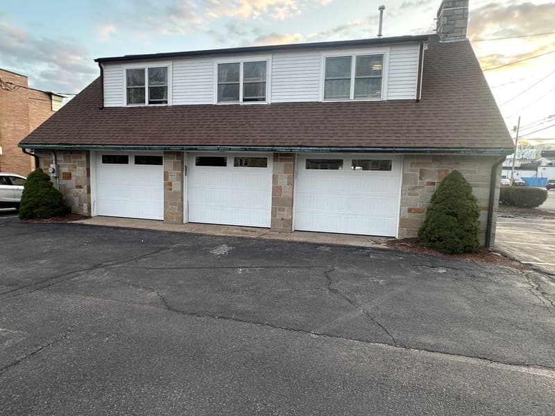 Triple white garage doors with transom windows on stone-faced commercial building